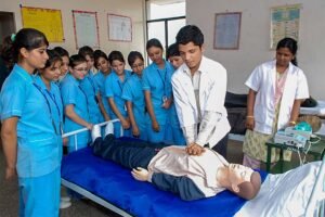 A doctor is teaching a nursing student at Nethaji Nursing College. The doctor is standing in front of a whiteboard and the student is sitting at a desk. The doctor is explaining a medical concept and the student is taking notes.